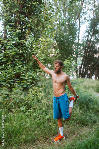 Sport fitness caucasian man with bare-chested stretching out in training in the forest.  Morning exercise in nature