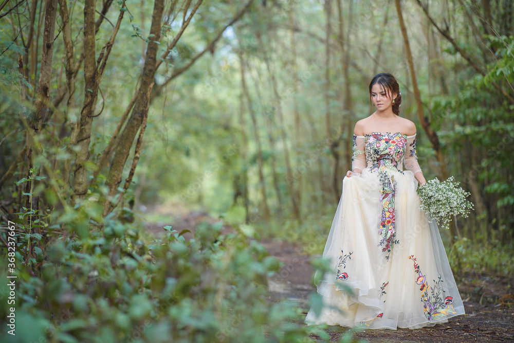 Portrait of young asian beautiful bride in white dress is posing on a wedding walk in the forest free from copy space.