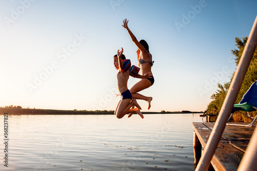 Single mother with her son enjoying on vacation jumping in lake from pier on summer day.