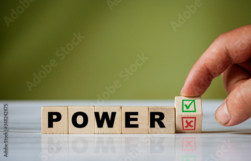The hand turns the wooden cube and changes the word POWER with green positive tick check box and red reject X check box.