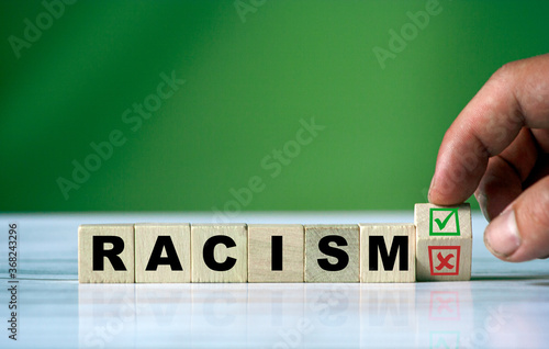 The hand turns the wooden cube and changes the word RACISM with green positive tick check box and red reject X check box. Yes or no.