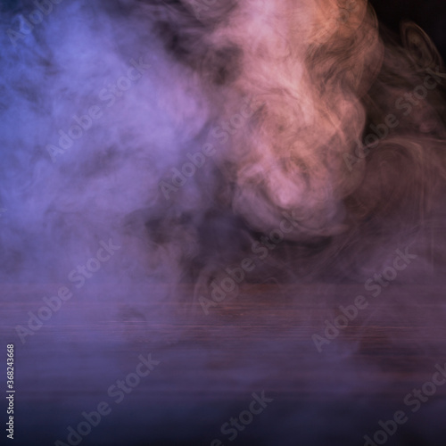 Conceptual image of multi-colored smoke isolated on dark black background and wooden table.