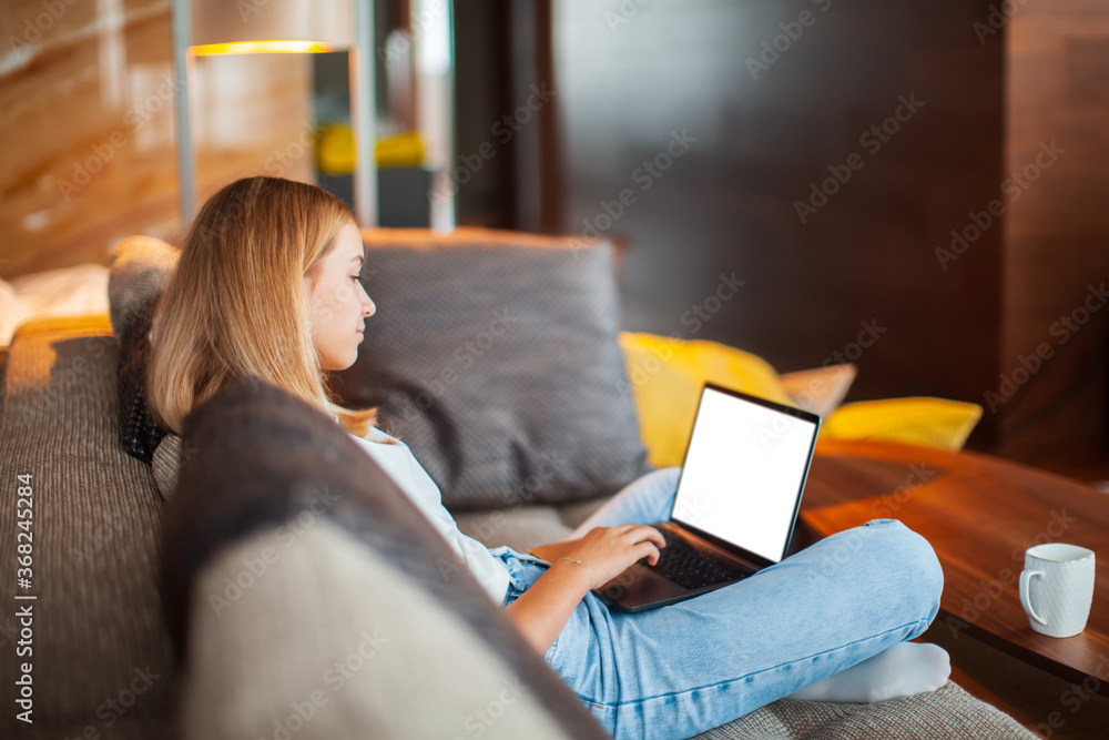 Teen girl sitting on sofa in Lotus position with blank screen laptop ...