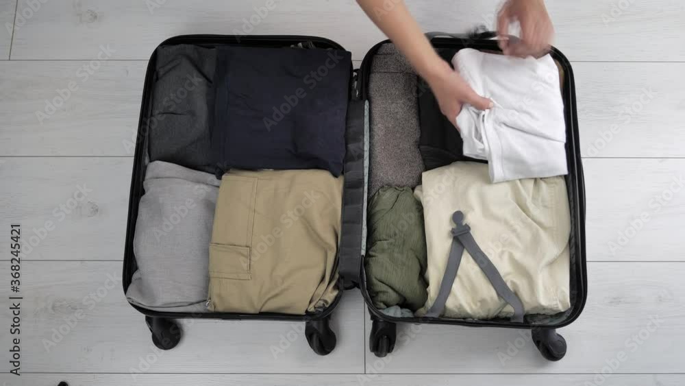 Close-up of a woman helping to pack a suitcase for her husband on a business trip. A woman puts beige clothes in a bag or suitcase on the floor. Slow motion. 4k Close-up of a woman helping to pack a suitcase for her husband on a business trip. A woman puts beige clothes in a bag or suitcase on the floor. Slow motion. 4k