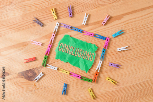 Conceptual hand writing showing Conclusions. Concept meaning explanation that uses data to support or reject a hypothesis Colored crumpled papers wooden floor background clothespin photo