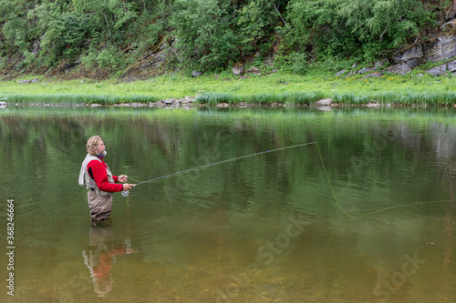 Elderly fisherman in water threw fishing rod. Fly fishing in mountain river.
