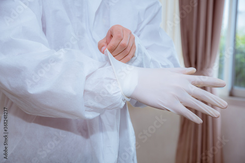 Close-up doctor wearing safety uniform and white surgical glove to protection virus from patient in hospital.