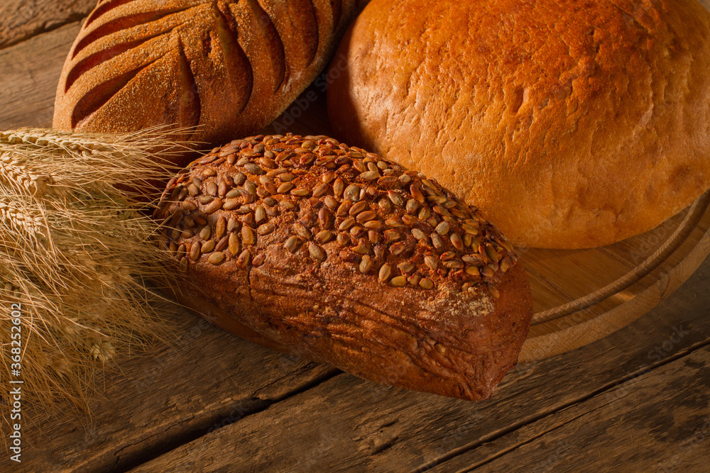 Fresh bread and wheat ears on wooden background. Fresh whole grain bread on cutting board.