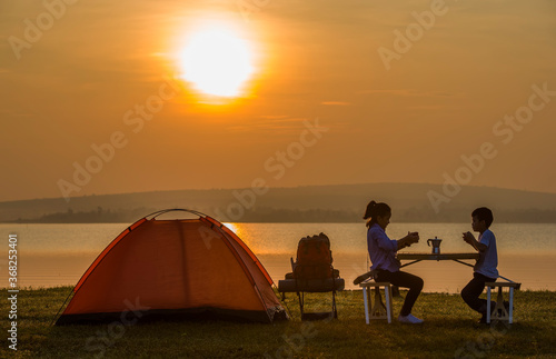 Girl and boy Sit and sip coffee in the morning beside the tent near the dam.