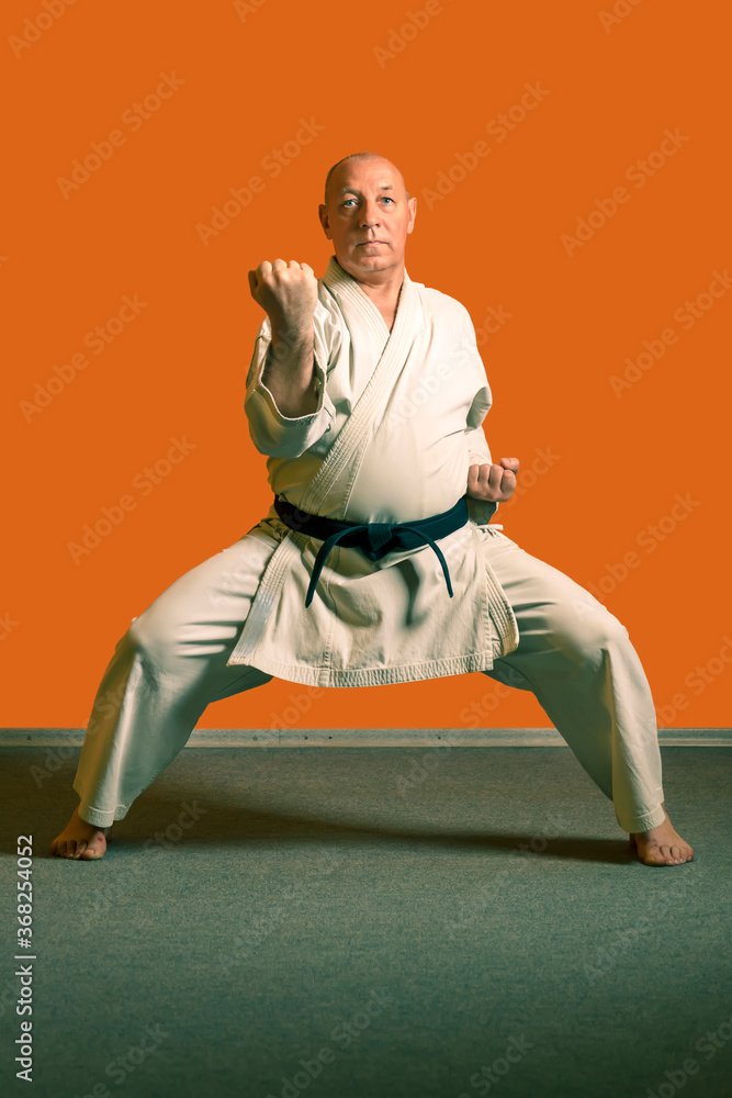 A karate man in a white kimono with a black belt does kata exercises.