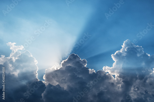 Sunbeams through a dark cumulus cloud in a blue sky