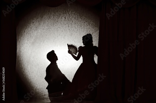 
People in medieval costumes in the theater of shadows on the stage with colored curtains. The theme of the love triangle