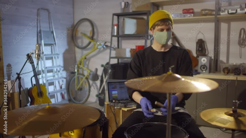 Unrecognizable man wearing mask on face putting on protective latex gloves and starting playing drums in studio Unrecognizable man wearing mask on face putting on protective latex gloves and starting playing drums in studio