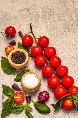 Ripe cherry tomatoes, garlic, basil, salt and black peppercorns on a stone culinary background
