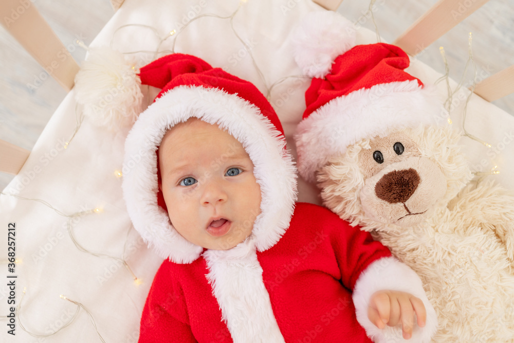 Christmas photo of a baby in a Santa costume lying in a crib at home with a toy in a Santa Claus hat, top view, happy new year Christmas photo of a baby in a Santa costume lying in a crib at home with a toy in a Santa Claus hat, top view, happy new year