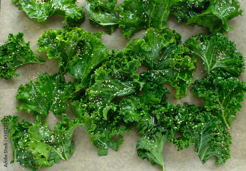 Sliced fresh curly kale with salt, pepper and sesame seeds on brown baking paper.