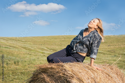 Adult woman enjoying the sun, climbing on a bale of straw