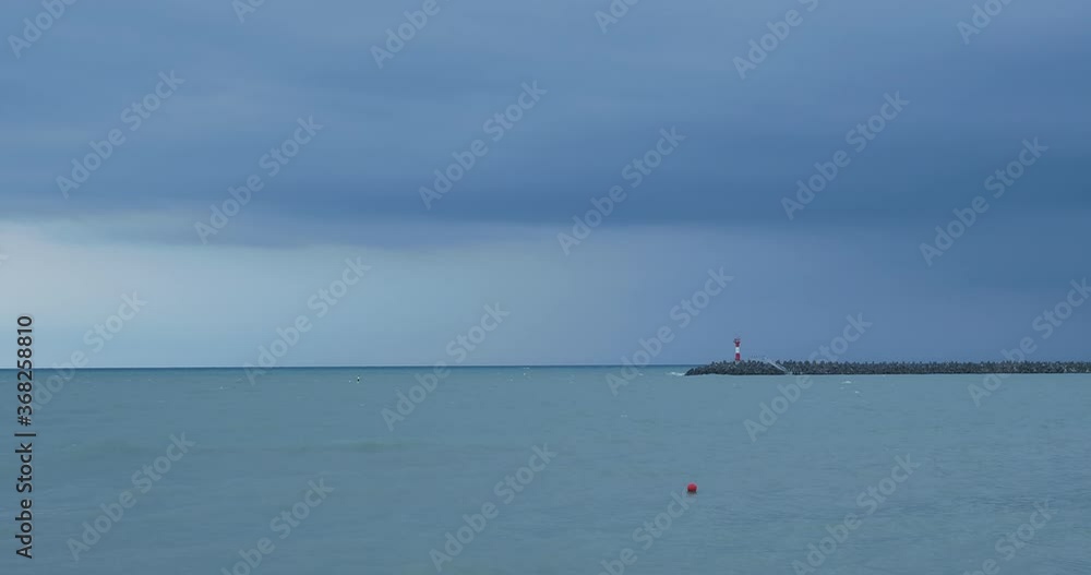Seagulls and cormorants sit on breakwater. Lighthouse on stormy sky background. Port of Sochi, Russia. Seagulls and cormorants sit on breakwater. Lighthouse on stormy sky background. Port of Sochi, Russia.