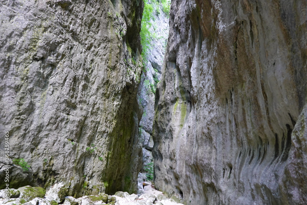 person walking between high rocks on a riverbed person walking between high rocks on a riverbed