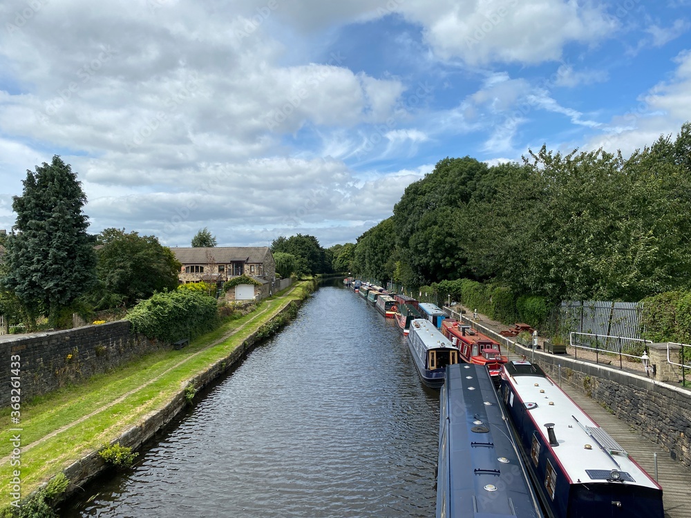 Boats on the Calder and Hebble canal, with trees and buildings in the distance near, Mirfield, Yorkshire, UK