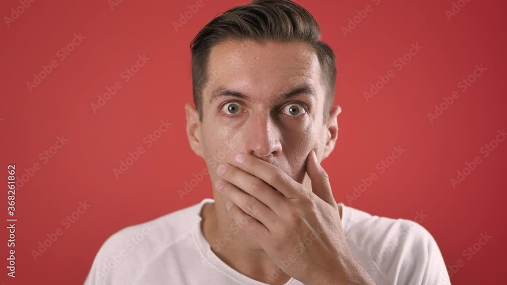 Stylish young man shocked and surprised on red color background. Man hipster in surprise shoots sunglasses and looks at the camera in surprise in slow motion Stylish young man shocked and surprised on red color background. Man hipster in surprise shoots sunglasses and looks at the camera in surprise in slow motion