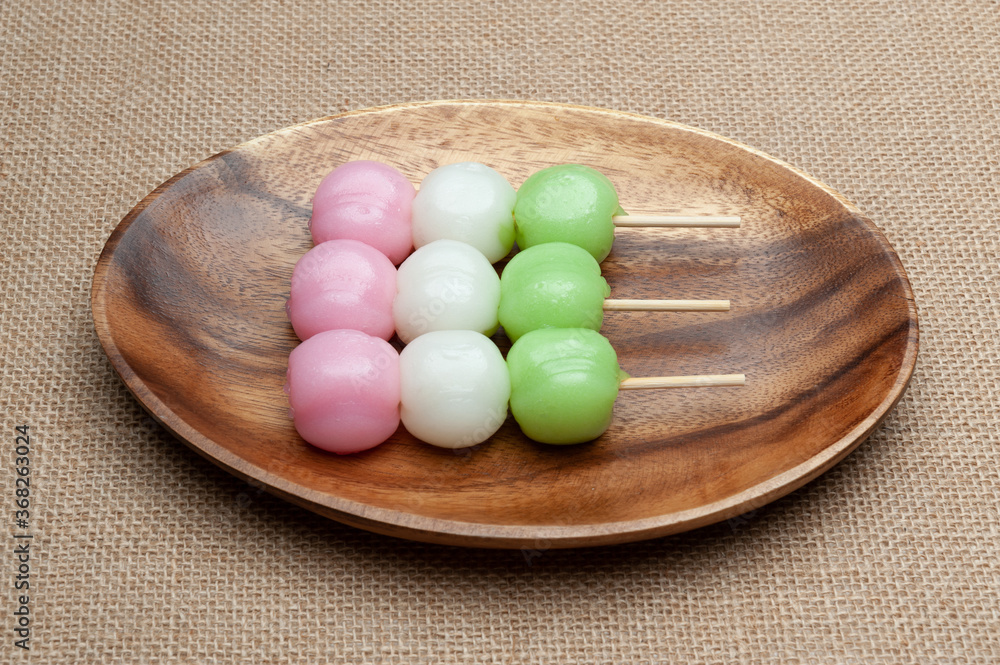 Japanese traditional sweet called Dango Mochi on wooden platter with green tea. Isolated on jute background. Close-up. Top view. Horizontal shot. Japanese traditional sweet called Dango Mochi on wooden platter with green tea. Isolated on jute background. Close-up. Top view. Horizontal shot.