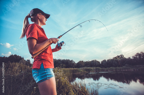 Leinwand Poster Cute woman is fishing with rod on lake