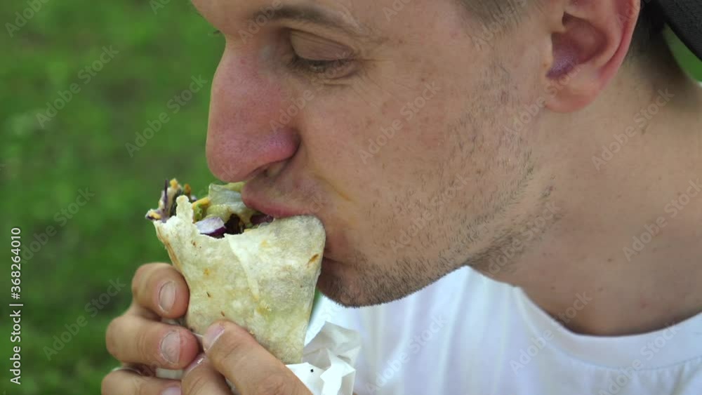 Man eating vegan wrap and licks his lips. Street food concept. Man eating vegan wrap and licks his lips. Street food concept.