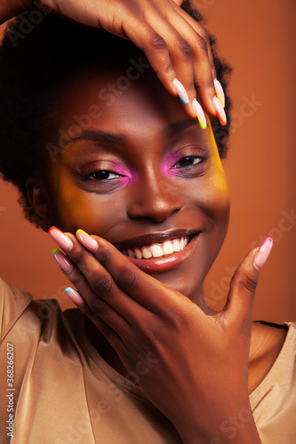 young pretty african girl with bright colorful makeup and manicure posing cheeful on brown background, lifestyle people concept