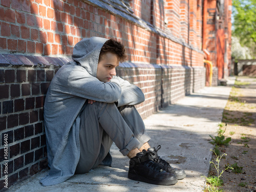 A lonely, sad teenager sits alone on the street near the house. quarrel with parents, problems at school. problems and psychology of adolescents, concept