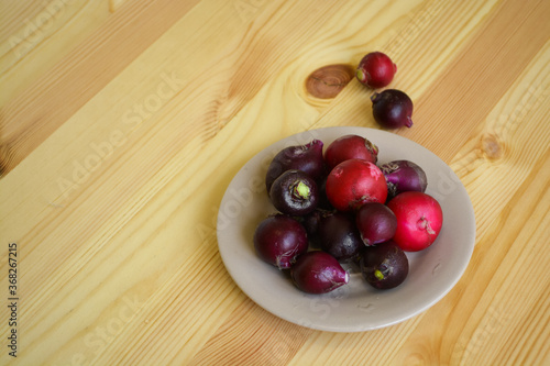 Many colorful raw radish in brown plate, bright purple vegetables on wooden table. Healthy vegetarian and organic kitchen concept