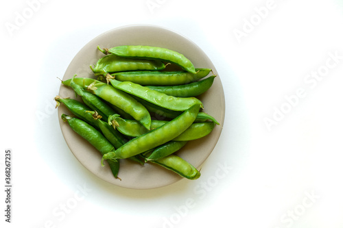 A pile of raw green peas in brown plate, fresh harvest from garden. Healthy vegetarian food concept, isolated on white background