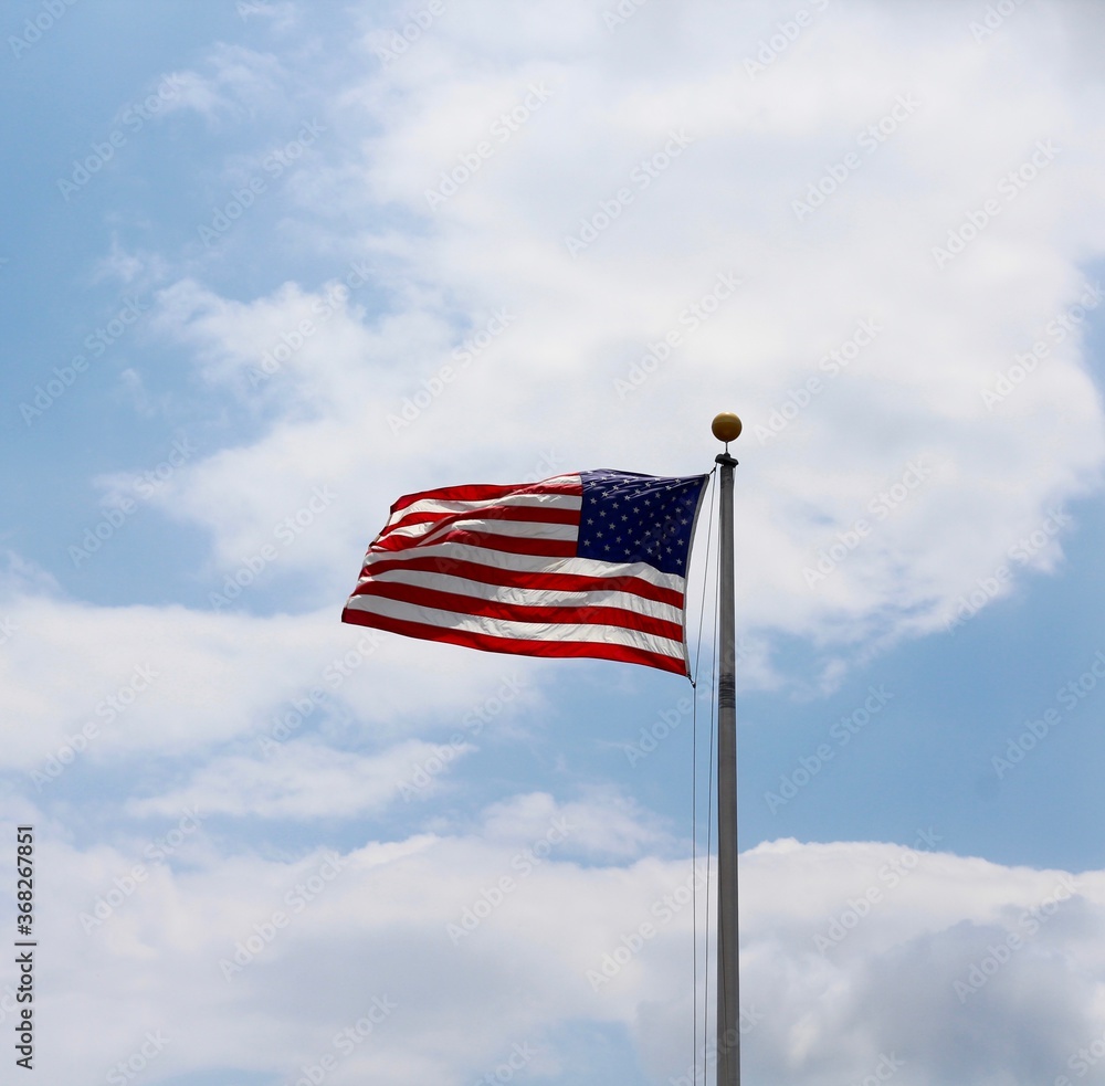 The american flag with the white clouds and blue sky.