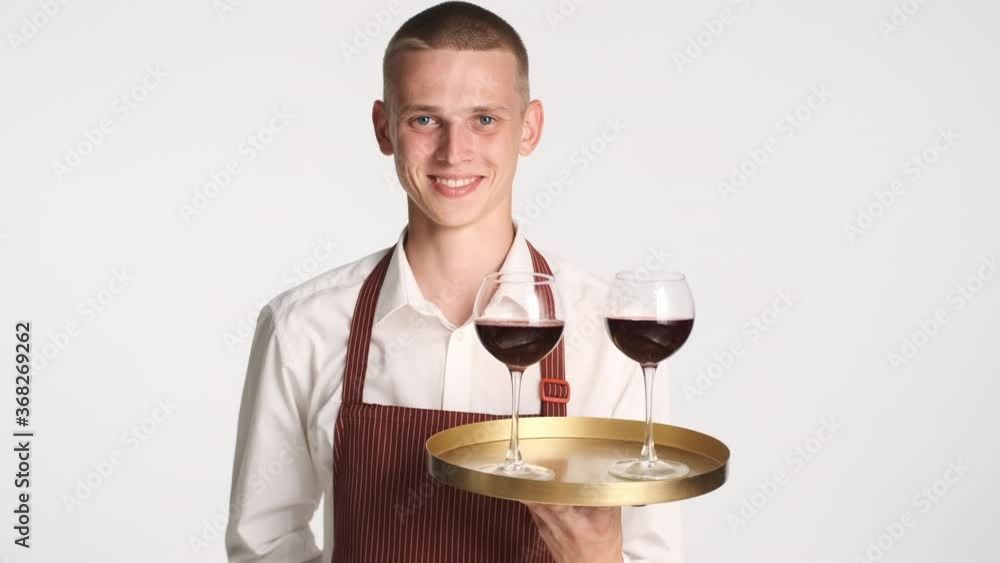 Young handsome confident waiter holding tray with red wine happily looking in camera isolated Young handsome confident waiter holding tray with red wine happily looking in camera isolated