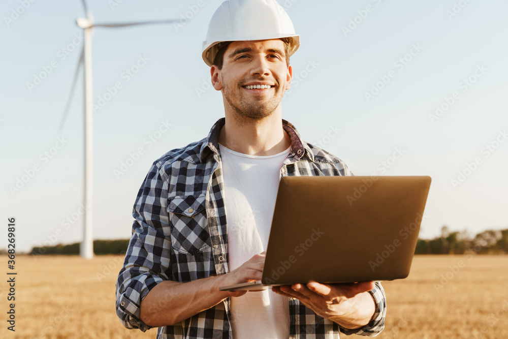 An electrical engineer standing on a field with windmills An electrical engineer standing on a field with windmills