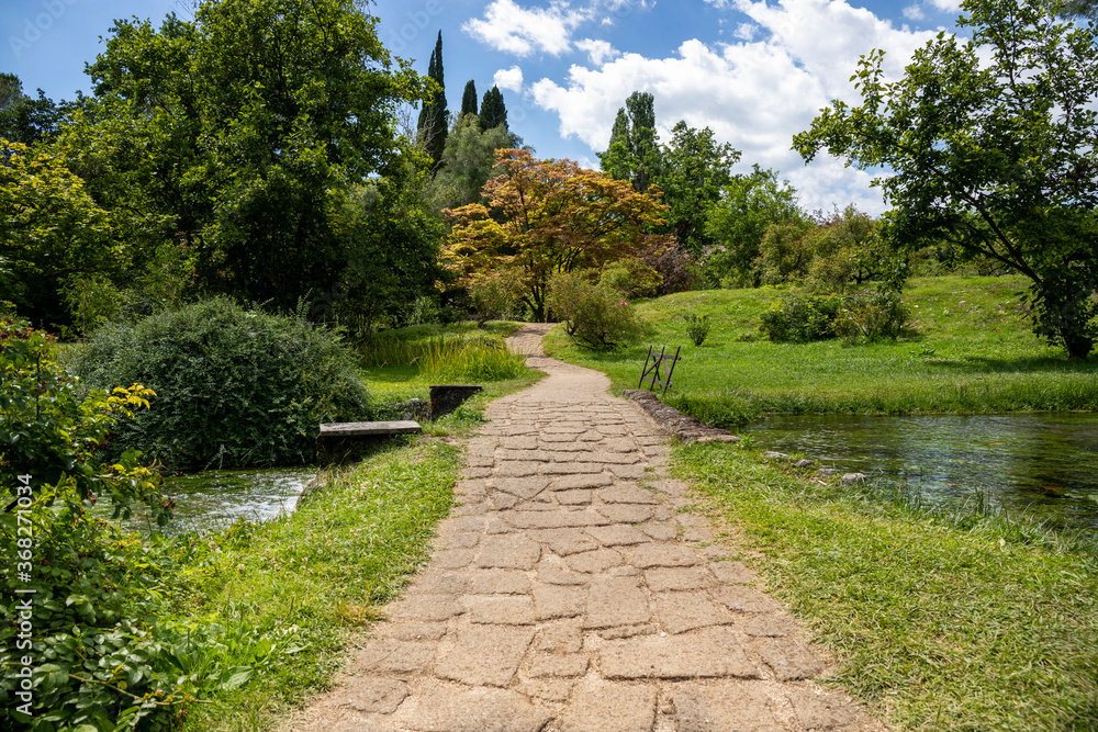 Obraz premium Garden of Ninfa and the pathway made with cobblestones, in Italy in the province of Latina. Most beautiful and romantic gardens in the world.