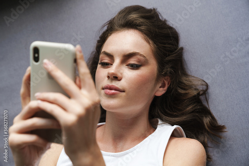 Image of beautiful focused woman using mobile phone while lying