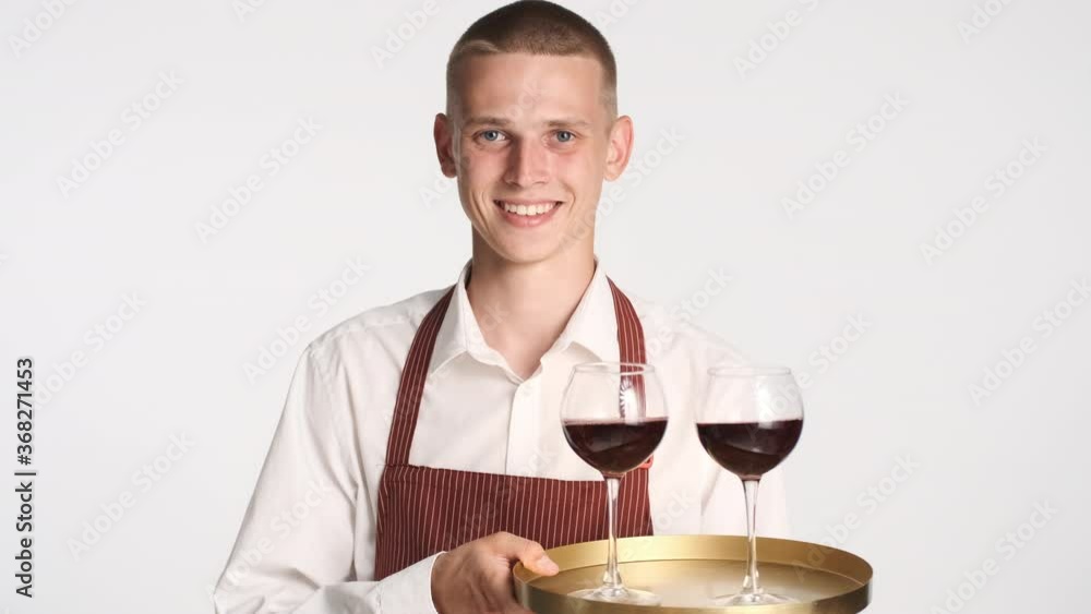 Young attractive smiling waiter in apron holding tray with red wine over white background Young attractive smiling waiter in apron holding tray with red wine over white background