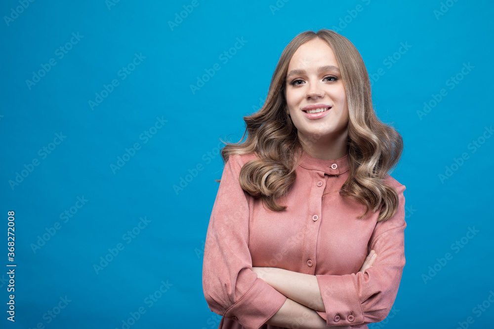 Portrait of happy woman standing with hands folded isolated on blue background in pink dress with blond hair Portrait of happy woman standing with hands folded isolated on blue background in pink dress with blond hair