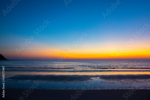 Colorful sea beach sunrise with deep blue sky and sun rays.