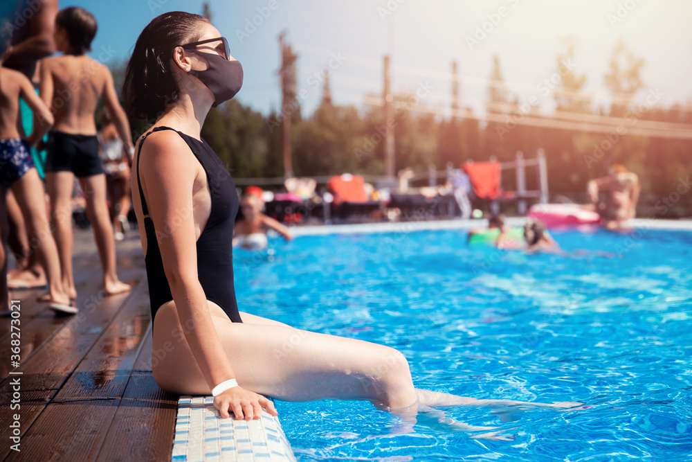 Woman in black protective mask from coronavirus bathes in hotel pool, summer epidemic vacation. Social distance concept