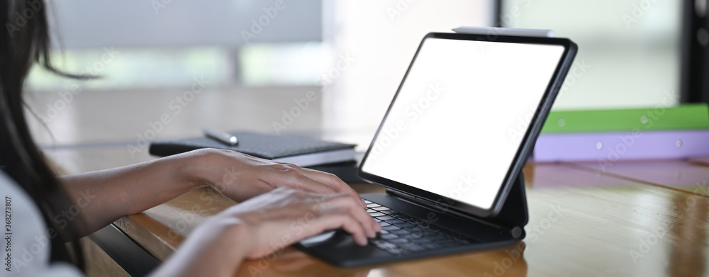 A cropped image of a woman's hand is using a computer tablet at the wooden working desk. A cropped image of a woman's hand is using a computer tablet at the wooden working desk.
