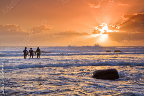 Three surfers sum up the waves at sunrise. photo