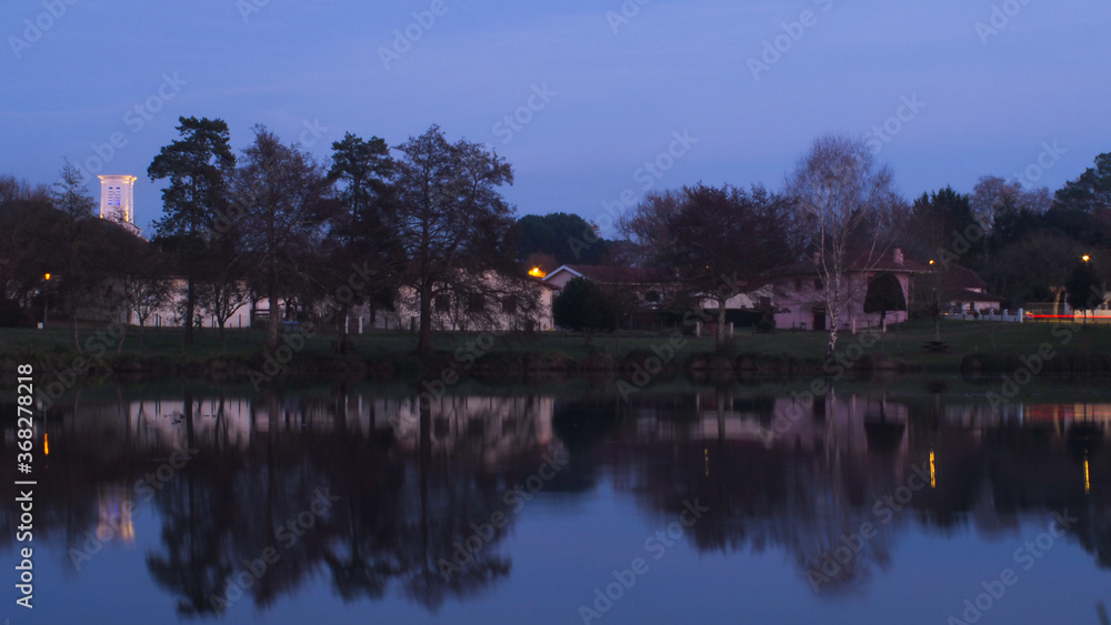 Pose longue d'un étang, par-dessus lequel trône le clocher du village, illuminé à sa base