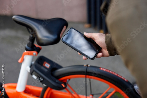 Man using mobile phone to unlock two-wheeled bike-sharing vehicle in city photo