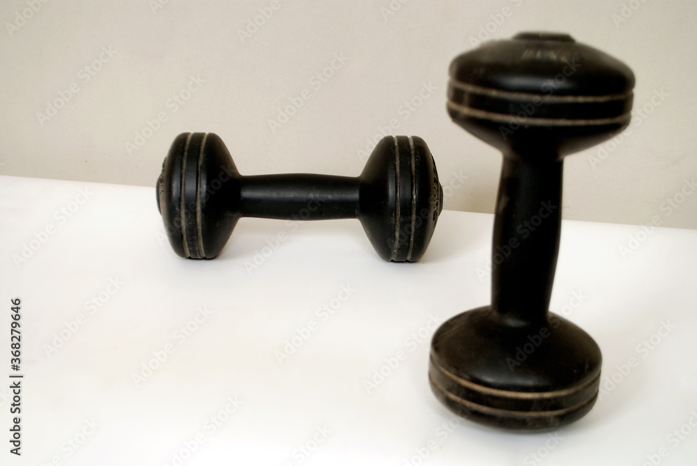 A pair of black workout dumbbells isolated on white ground and grey wall using soft and selective focus . A pair of black workout dumbbells isolated on white ground and grey wall using soft and selective focus .