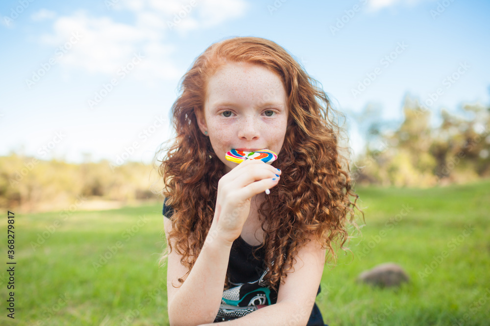 Young girl outside eating a rainbow lollipop Young girl outside eating a rainbow lollipop