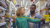 Young multiethnic couple in hardware store using measuring tape