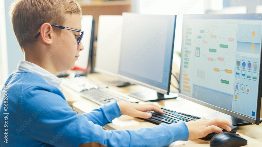 Elementary School Computer Science Classroom: Cute Little Boy wearing Glasses Uses Personal Computer, Learning Programming Language for Software Coding, Over the Shoulder Shot