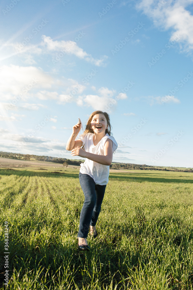 Young girl flying a paper aeroplane in a green farm paddock